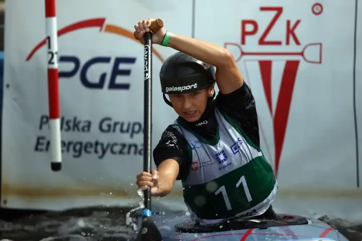 Młody mistrz polski w kajakarstwie, w kasku i kamizelce z numerem 11, wiosłuje w wodzie.